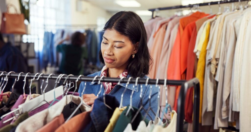 Shopping, search or woman in store with clothing rack, outfit check or decision in trendy style. Retail, option or customer in boutique with rail, garment choice or selection in fashion purchase.